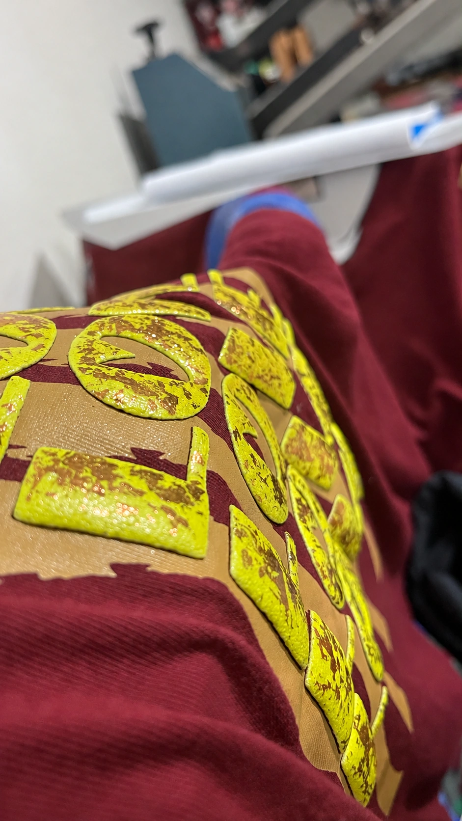 Detalhe de letras amarelas em relevo com efeito puff e foil dourado sobre tecido vinho